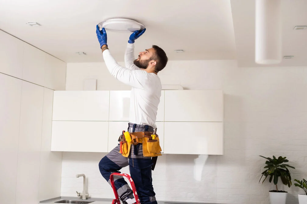 A Rhode Island electrician standing on a ladder doing a lighting fixture install